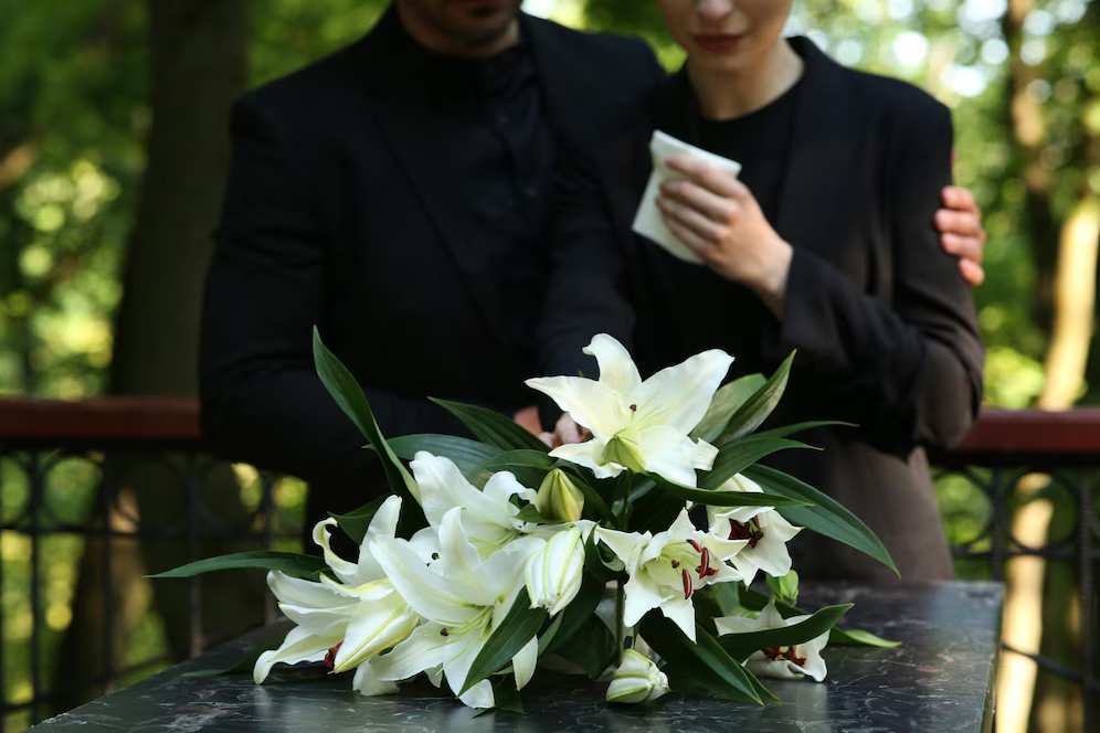 couple-near-granite-tombstone-with-white-lilies-cemetery